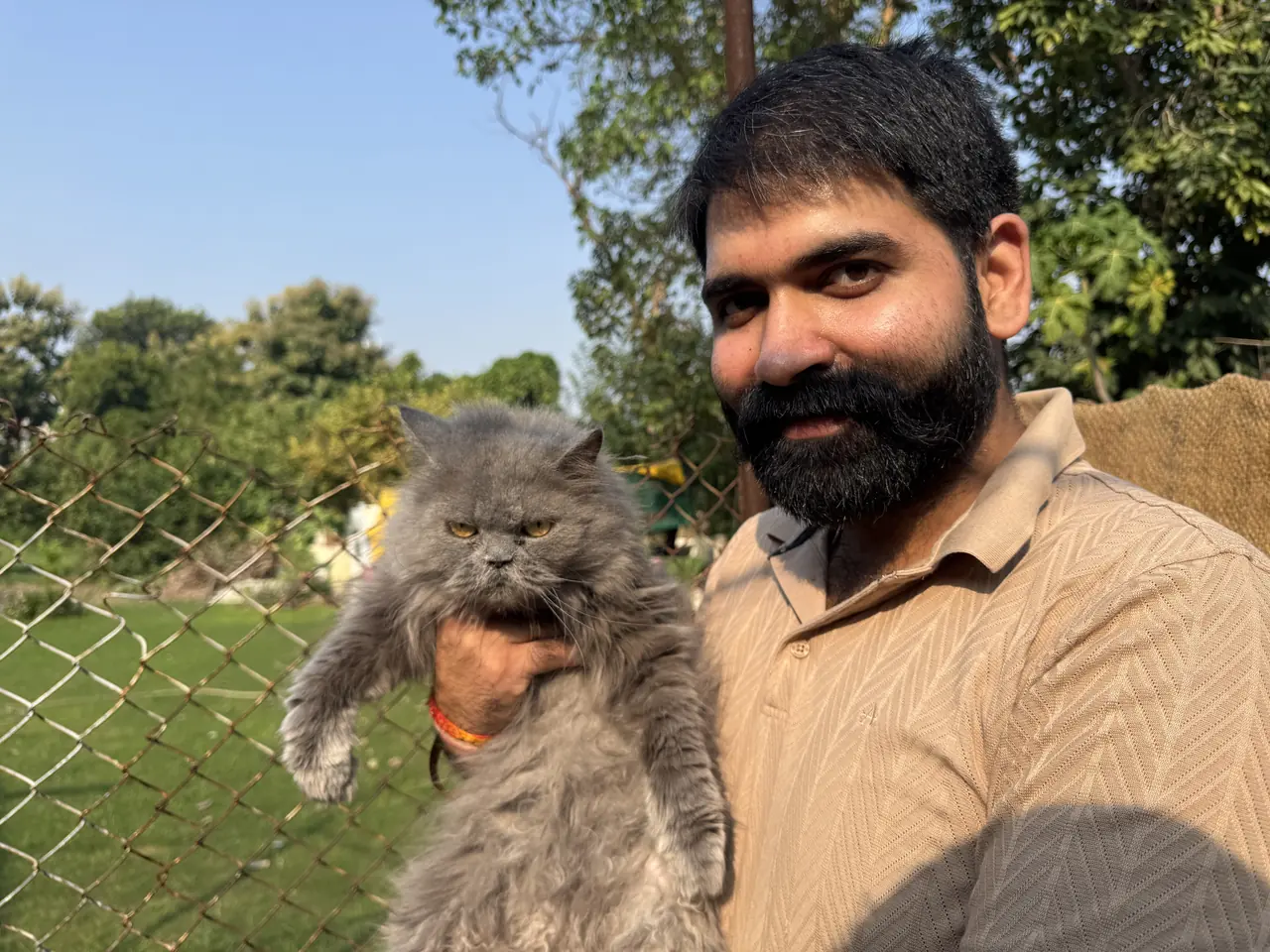 Nikhil holding a grey Persian cat at the farm fence